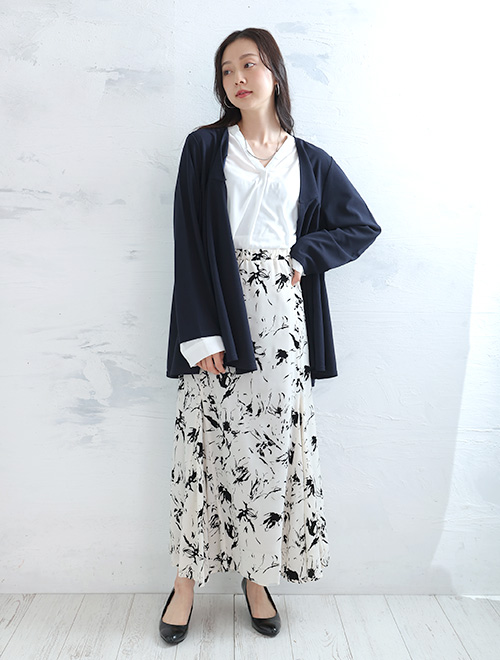 白シャツにネイビーのジャケットを羽織り、柄スカートを履く女性