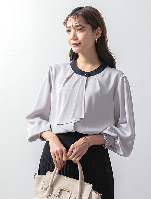 スカーフタイデザインのブラウスを着て、黒のプリーツスカートを履いた女性