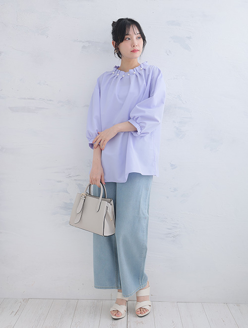 パールネックブラウスを着て、デニムパンツを履く女性