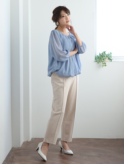 ブルーのバルーンブラウスを着て、ベージュのパンツを履く女性