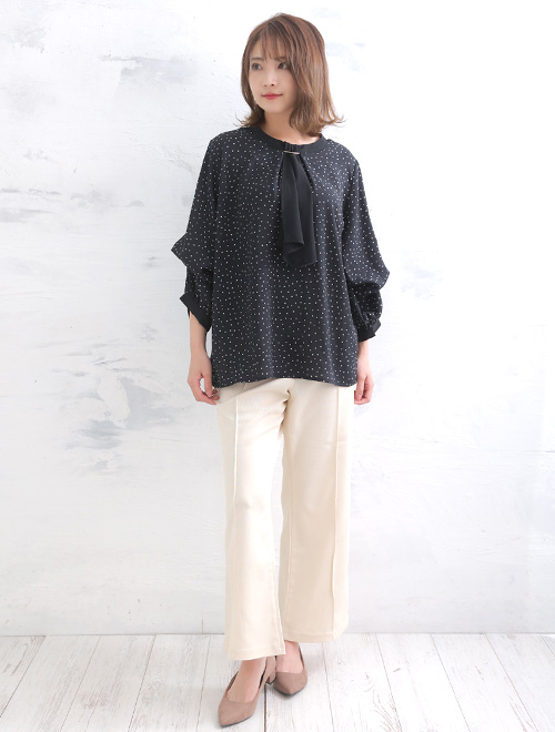 ドット柄ボウタイブラウスを着て、白のストレートパンツを履く女性
