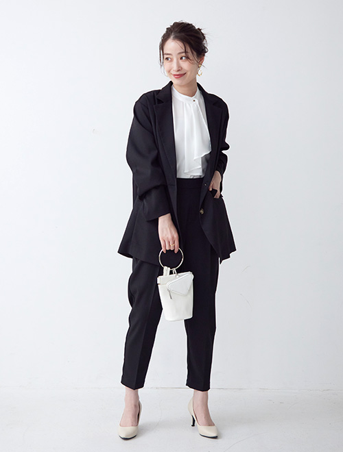 ボウタイブラウスにジャケットを羽織り、テーパードパンツを履く女性
