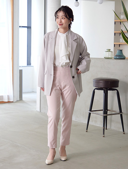 ボウタイブラウスにグレーのジャケットを羽織り、ピンクのテーパードパンツを履く女性