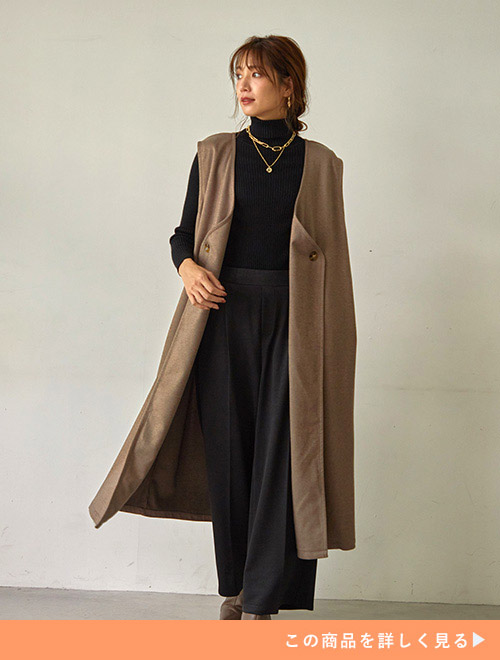 黒のワントーンコーデに、モカ色のロング丈ベストを羽織る女性