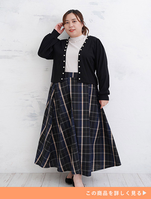 チェック柄ロングスカートに白トップスをインして、黒のパール付きカーディガンを羽織る女性