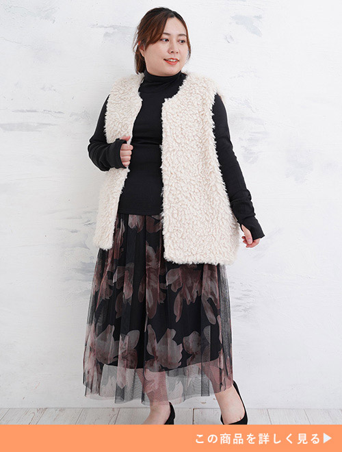 黒トップス×花柄チュールスカートに、アイボリーのファーベストを羽織る女性