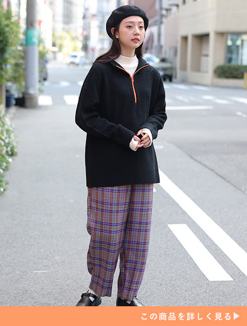 白系トップスに黒プルオーバーを重ね着して、パープル系のチェック柄パンツを履く女性