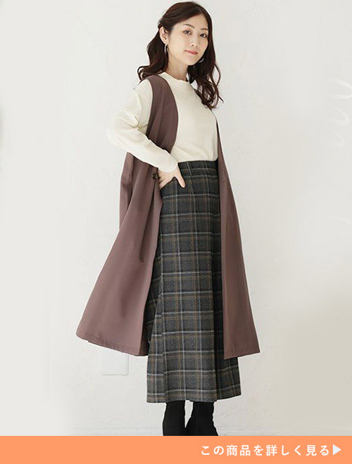 白系トップス×チェック柄ボトムに、モカ色のロング丈ジレを羽織る女性