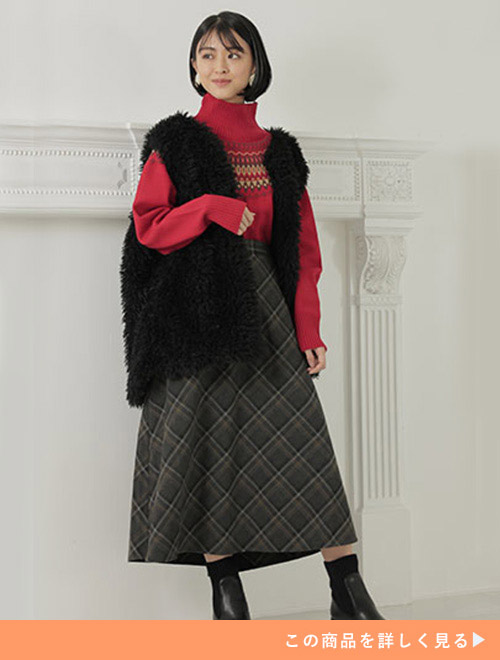 赤色のセーター×チェック柄フレアースカートをトップスインで着て、黒のファーベストを羽織る女性