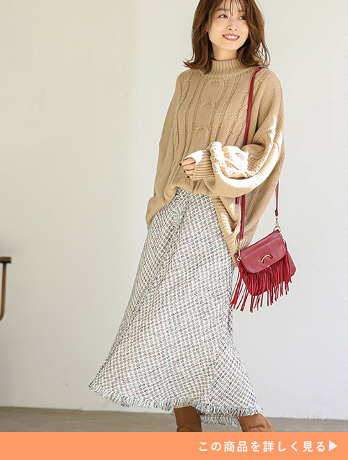 赤×グレーのロング丈タイトスカートに、ベージュのニットを前だけトップスインして着る女性