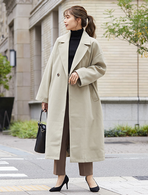 黒のボトルネックニット×茶のパンツに、グレージュのチェスターコートを羽織る女性