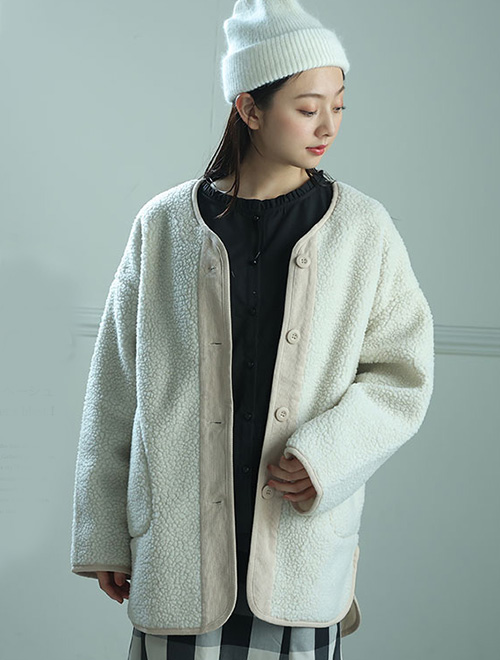 黒トップス×白黒ブロックチェック柄スカートに、ライトベージュのボアジャケットを羽織る女性