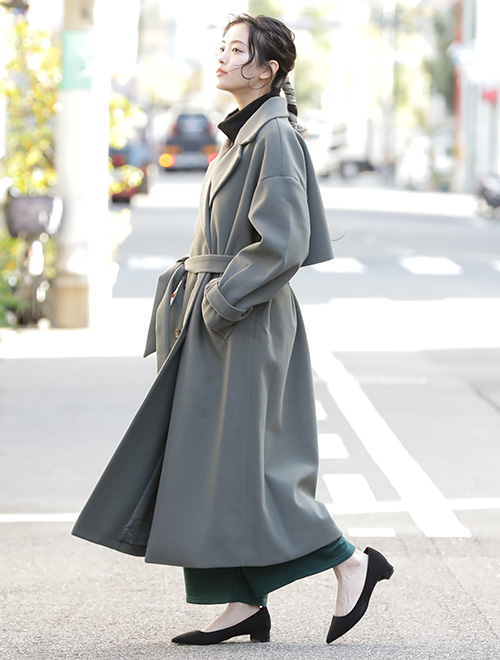 黒トップス×深緑ボトムに、くすみグリーンのロング丈トレンチコートを羽織る女性