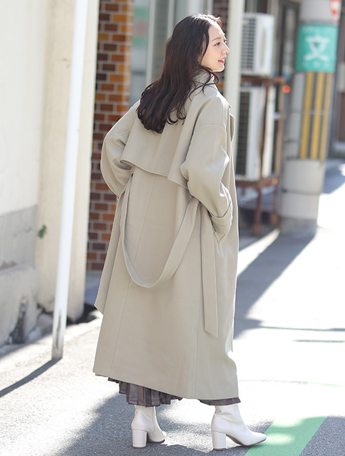 大きめのバックヨークがあるライトグリーンのトレンチコートを着て、後ろを振り返る女性