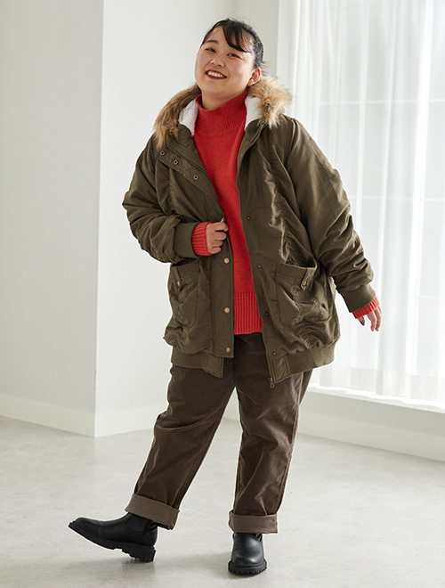 朱赤色ニット×茶色パンツコーデに、カーキのモッズコートを羽織る女性。