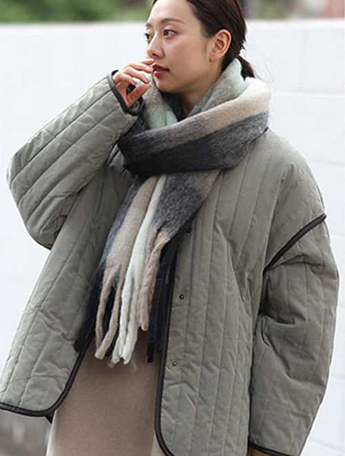 カーキのキルティングジャケットを羽織り、ボリュームのあるマフラーを首に巻く女性