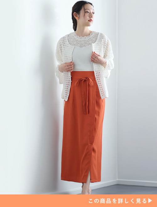 アラゴンオレンジのタイトスカートにホワイトトップスとカーディガンを羽織る女性