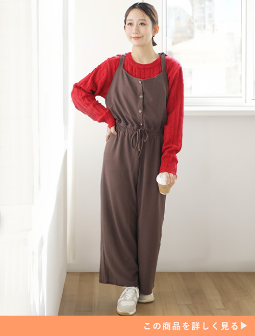 モカのサロペットとレッドカラーのケーブル編ニットのコーデにホワイトスニーカーを履く女性