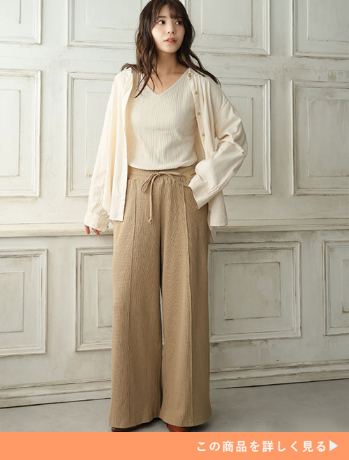 グレージュのワッフルシルエットのワイドパンツにアイボリーのトップスとカーディガンを合わせる女性