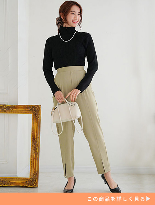 オリーブの裾スリット入りテーパードパンツにブラックのタートルニットを合わせる女性