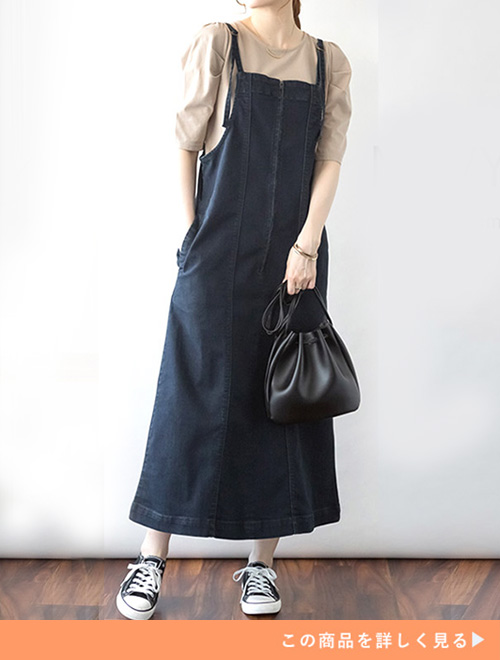 ベージュトップスにデニムのジャンバースカートのコーデにスニーカーを履く女性