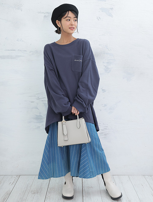 ネイビーのトップスと水色のスカートに白いカバンを持つ女性