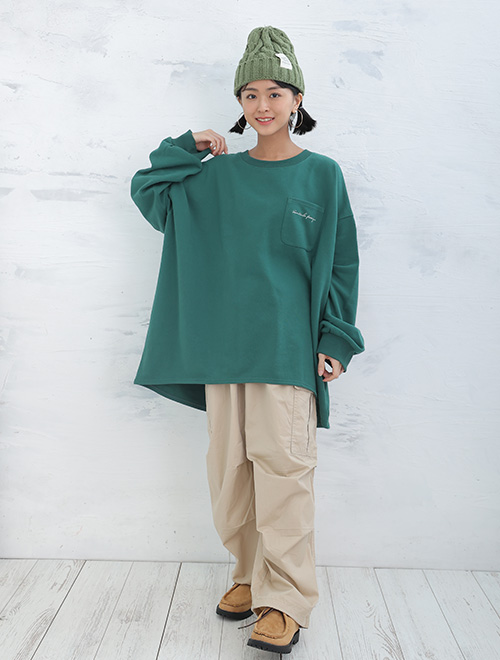 グリーンのトップスにベージュのボトムスを履いた女性が右手を右肩に置いている