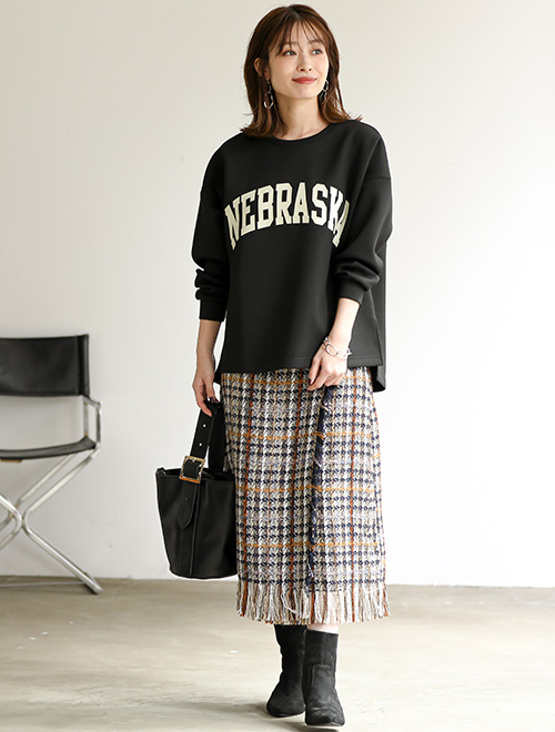 ロゴ入りのブラックトップスとタイトなツイードのスカートを着た女性