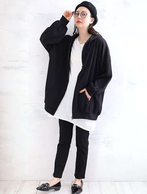 黒いトップスとボトムスを着た女性が右手でメガネを押さえている