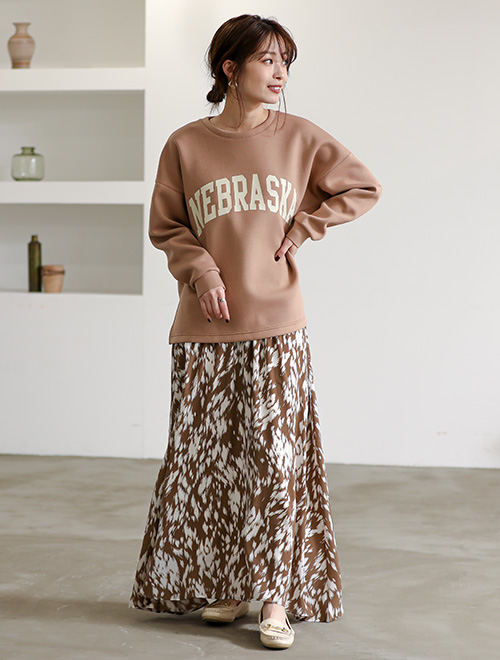 ロゴトレーナーとブラウンの柄スカートを履いた女性