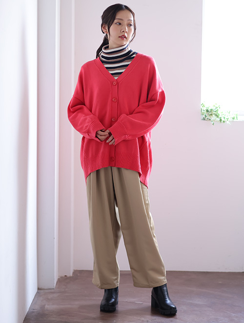 ボーダーのハイネックトップスにピンクのカーディガンを重ね、ベージュのボトムスを着た女性