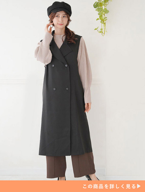 ベージュのニットにブラウンのパンツ、黒いジレを着た女性