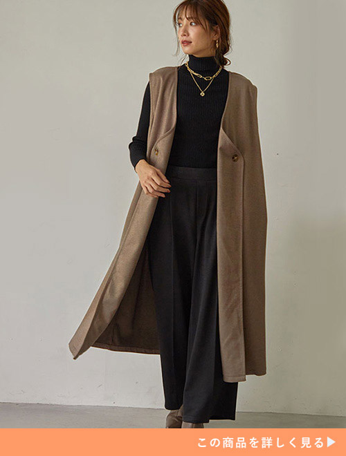 ブラックのコーデにベージュのジレを羽織った女性