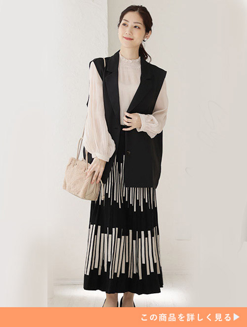 モノトーンの柄スカートにシフォンブラウス、黒いジレを羽織った女性