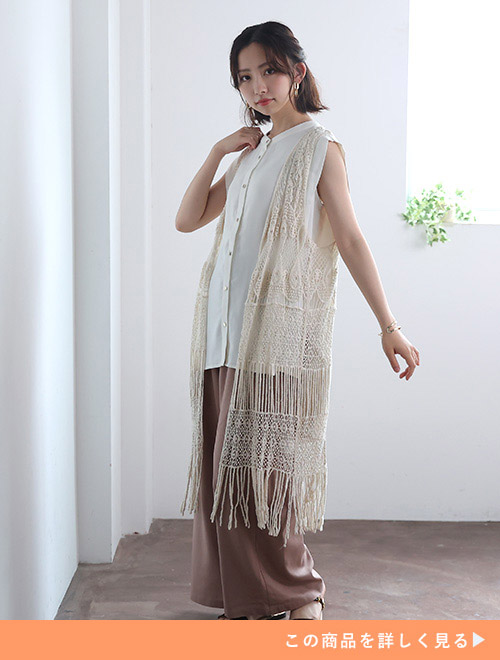 右手を肩に添えて左手を広げるレースのジレを着た女性