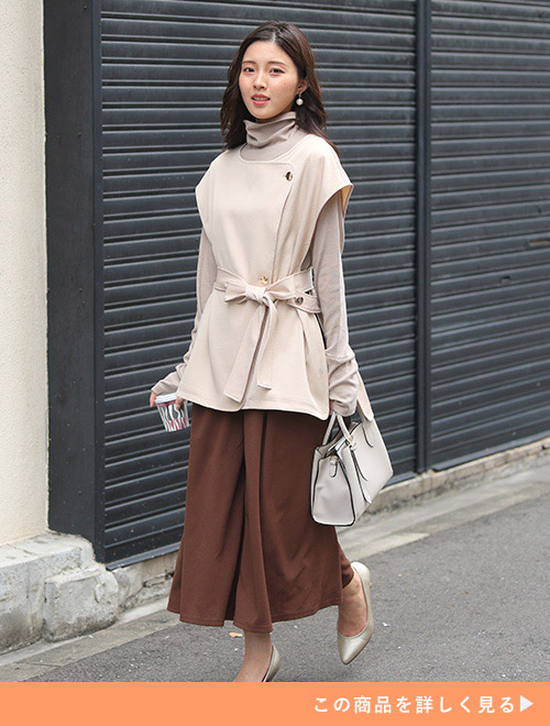 ブラウンのフレアボトムにベージュのハイネックニット、アイボリーのジレを羽織った女性