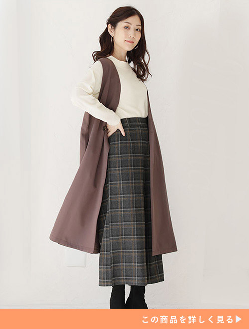 ピンクベージュのジレにチェックのロングタイトスカート、白のトップスを着た女性