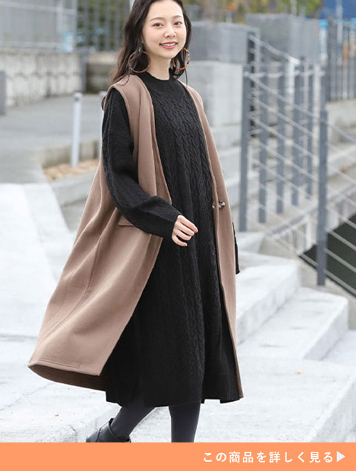 黒のニットワンピースにベージュのジレを着た女性