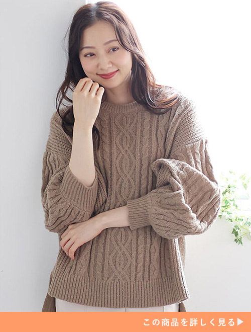 ベージュのニットとホワイトカラーのパンツを着てほほえむ女性