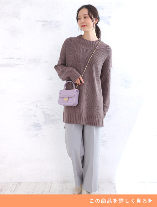 くすみカラーのパープルニットにグレーのパンツを着た女性