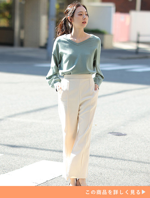 グリーンのVネックニットに白パンツを合わせた女性