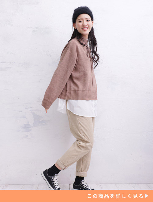 シャツをINしたようなピンクのレイヤード風ニットにベージュパンツを着た女性