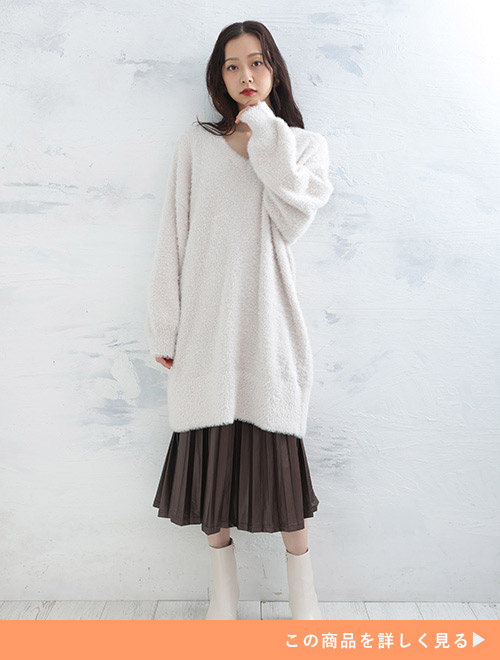 白いシャギーニットにブラウンのプリーツスカートを履く女性