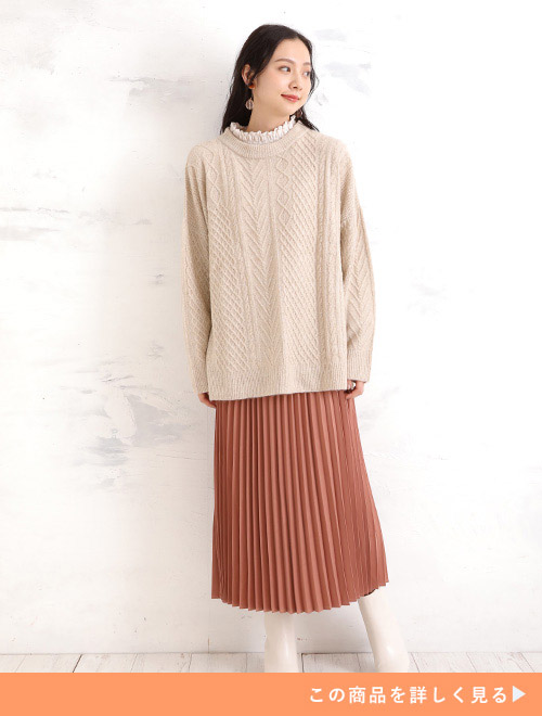 白いニットにオレンジ色のプリーツスカートを履く女性