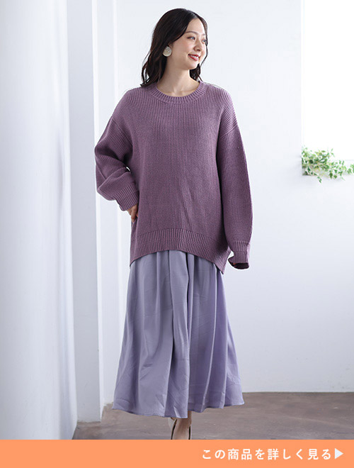 ラベンダーカラーのニットにツヤ感のあるロングスカートを履く女性