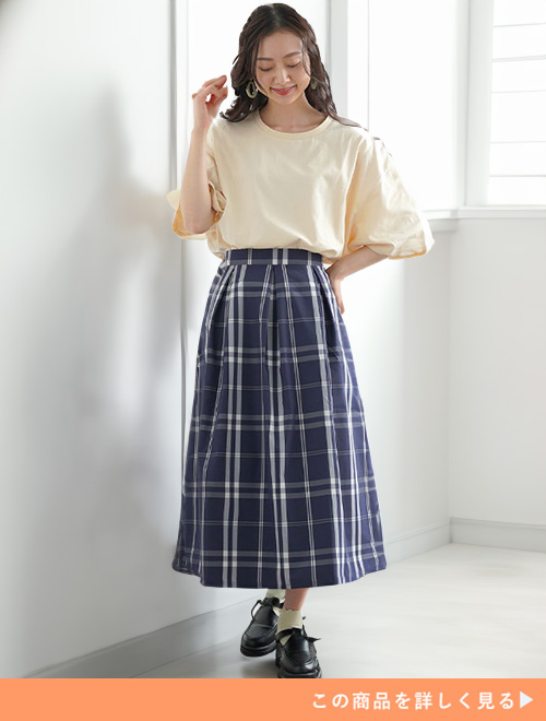 クリーム色のブラウス×ブルーのチェック柄スカートを着る女性