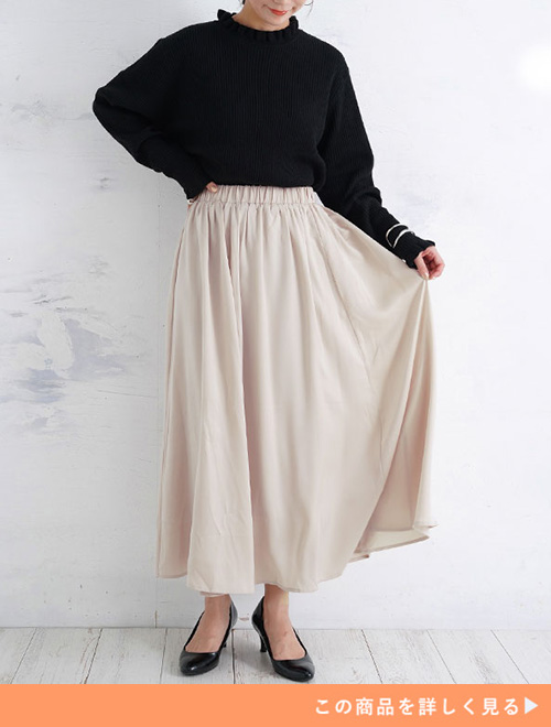 黒トップス×ベージュのサテン地フレアースカートを着る女性