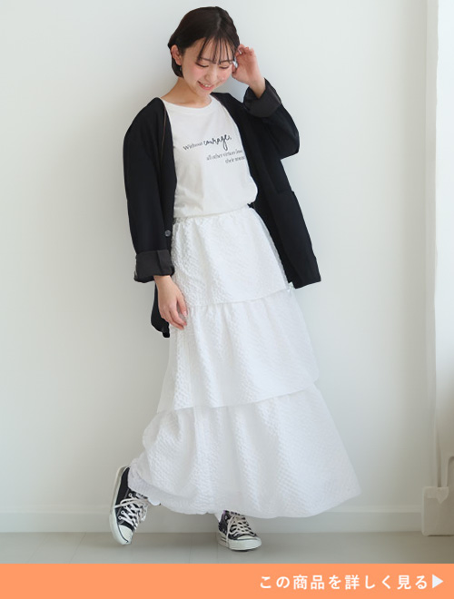 白のロゴT×白のティアードスカートに黒のカーディガンを羽織る女性。