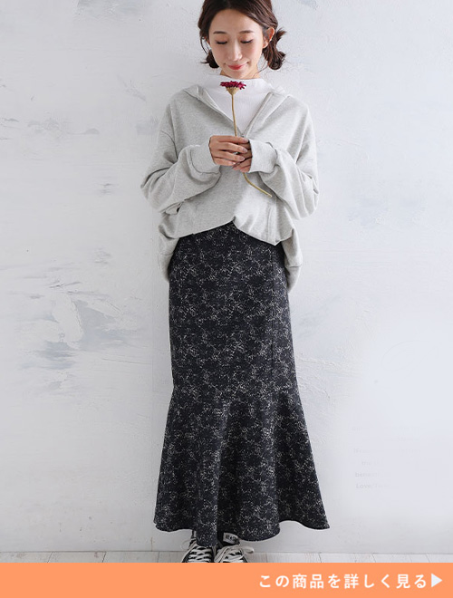 白のレーストップスにグレーのパーカを重ね着し、黒の小花柄スカートを履く女性