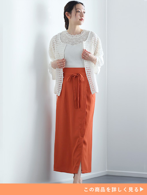白のレーストップスにレースカーディガンを重ね着し、オレンジのたいとスカートを履く女性